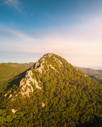 Aerial view of a rocky mountain peak with limestone ridges and dense green forests under a clear blue sky in Rijeka Primorje Gorski Kotar Croatia. Aerial view of a rocky mountain peak with limestone ridges and dense green forests under a clear blue sky in Rijeka Primorje Gorski Kotar Croatia.