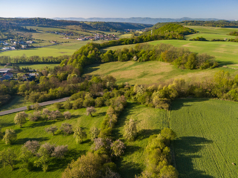 Aerial view of lush green rolling hills and agricultural fields with a small village nestled in the valley under a clear blue sky Cerin Banskobystricky kraj Slovakia. Aerial view of lush green rolling hills and agricultural fields with a small village nestled in the valley under a clear blue sky Cerin Banskobystricky kraj Slovakia.