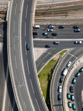 Aerial view of a highway interchange with multiple lanes of traffic railway tracks and green spaces in Alges Lisbon Portugal.
