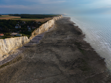 Aerial view of the Beach of the Bois de Cise featuring white chalk cliffs green vegetation and an expansive rocky shoreline at low tide in Ault Hauts de France France.