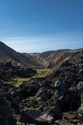 View of dark volcanic rocks and green moss contrasting with the golden mountains under a clear blue sky Rang&aacute;r&thorn;ing ytra Rang&aacute;r&thorn;ing ytra Iceland.
