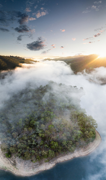 Aerial view of Kangaroo Creek Reservoir with thick morning fog rolling over forested hills and calm water during sunrise Adelaide Hills Council South Australia Australia. Aerial view of Kangaroo Creek Reservoir with thick morning fog rolling over forested hills and calm water during sunrise Adelaide Hills Council South Australia Australia.