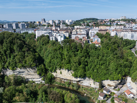 Aerial view of the Sarine river winding through steep sandstone cliffs and dense green forests below the historic city skyline Fribourg Fribourg Switzerland. Aerial view of the Sarine river winding through steep sandstone cliffs and dense green forests below the historic city skyline Fribourg Fribourg Switzerland.