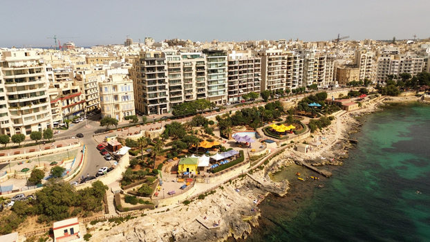 Aerial view of the coastal urban landscape in Sliema featuring modern apartment buildings a rocky shoreline a public park with colorful umbrellas and the turquoise sea in Malta. Aerial view of the coastal urban landscape in Sliema featuring modern apartment buildings a rocky shoreline a public park with colorful umbrellas and the turquoise sea in Malta.