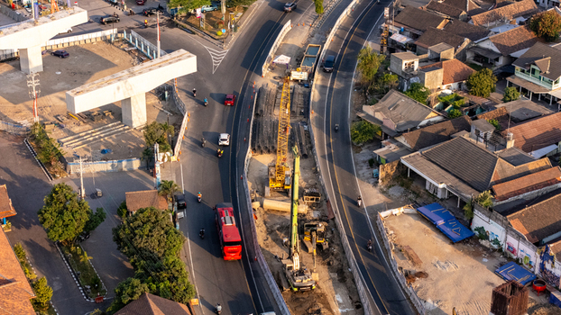 Indonesia 24 September 2026 Aerial view of a road construction site in an urban area showing a crane heavy machinery concrete pillars traffic and surrounding houses.