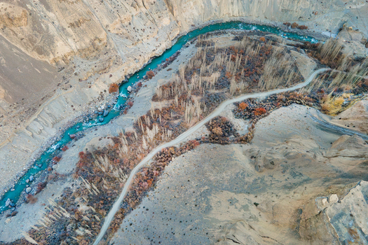 Aerial view of a vibrant turquoise river snaking through the rugged earthy terrain of Chapursan Valley a pathway hugging its curves Hunza Nagar Gilgit Pakistan. Aerial view of a vibrant turquoise river snaking through the rugged earthy terrain of Chapursan Valley a pathway hugging its curves Hunza Nagar Gilgit Pakistan.