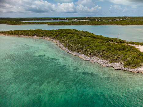 Aerial view of Crab Cay featuring turquoise waters rocky shorelines and lush tropical vegetation under a cloudy sky in Exuma Exuma The Bahamas. Aerial view of Crab Cay featuring turquoise waters rocky shorelines and lush tropical vegetation under a cloudy sky in Exuma Exuma The Bahamas.