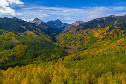 Aerial view of Capitol Peak and the Elk Range surrounded by vibrant autumn fall foliage and evergreen forests in the Rocky Mountains Snowmass Colorado United States.