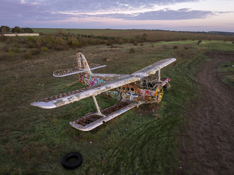Aerial view of an abandoned graffiti covered biplane resting in a grassy field under a soft sunset sky in Bulgaria. Aerial view of an abandoned graffiti covered biplane resting in a grassy field under a soft sunset sky in Bulgaria.