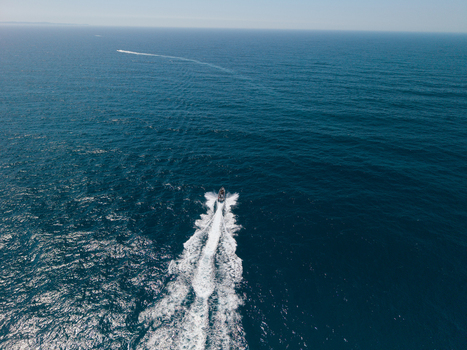 Aerial view of a small motorboat cutting through the deep blue ocean leaving a white wake behind it near Long Reef Headland in Collaroy New South Wales Australia.
