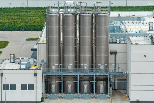 Aerial view of stainless steel agitation and mixing vessels at an industrial facility with a green field in the background in Poland. Aerial view of stainless steel agitation and mixing vessels at an industrial facility with a green field in the background in Poland.