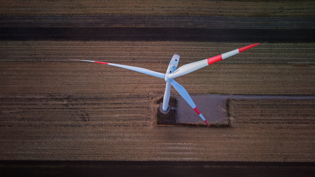 Aerial view of a wind turbine with red tipped blades standing in a vast agricultural field in Vladimirovac Vojvodina Serbia. Aerial view of a wind turbine with red tipped blades standing in a vast agricultural field in Vladimirovac Vojvodina Serbia.