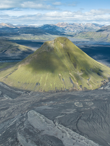 Aerial view of the iconic green Maelifell volcano rising from black volcanic sand plains surrounded by rugged mountains under a cloudy sky in Kirkjubaejarklaustur Skaftarhreppur Iceland. Aerial view of the iconic green Maelifell volcano rising from black volcanic sand plains surrounded by rugged mountains under a cloudy sky in Kirkjubaejarklaustur Skaftarhreppur Iceland.
