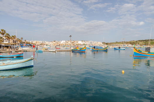 View of brightly colored traditional fishing boats bobbing gently on the tranquil deep blue water of the harbor Marsaxlokk Malta. View of brightly colored traditional fishing boats bobbing gently on the tranquil deep blue water of the harbor Marsaxlokk Malta.