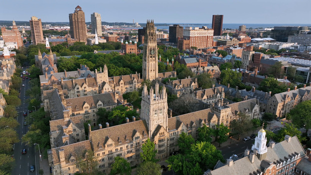 Aerial view of the historic Yale University campus featuring the iconic Harkness Tower surrounded by lush green trees and Gothic architecture in New Haven Connecticut United States.