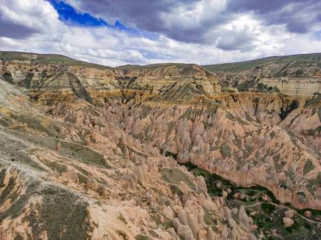 Aerial view of the dramatic rock formations and fairy chimneys of Zelve Valley featuring layered cliffs and arid terrain under a cloudy sky in Goreme Nevsehir Turkiye. Aerial view of the dramatic rock formations and fairy chimneys of Zelve Valley featuring layered cliffs and arid terrain under a cloudy sky in Goreme Nevsehir Turkiye.