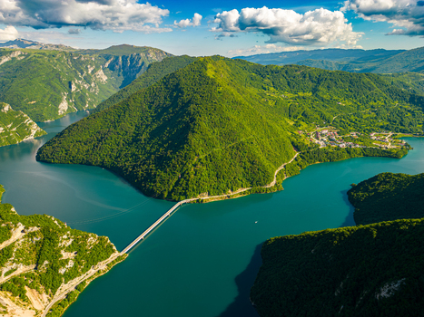 Aerial view of Piva Lake with its turquoise water a bridge crossing the narrow section and surrounding lush green mountains Pluzine Municipality Montenegro. Aerial view of Piva Lake with its turquoise water a bridge crossing the narrow section and surrounding lush green mountains Pluzine Municipality Montenegro.