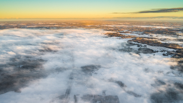 Aerial view of a vast snowy landscape blanketed by low lying clouds during the golden hour in Latvia. Aerial view of a vast snowy landscape blanketed by low lying clouds during the golden hour in Latvia.