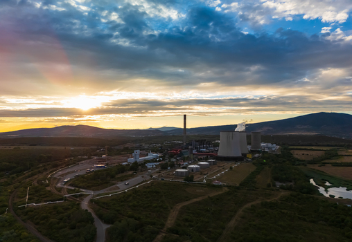 Aerial view of a lignite fired power plant with cooling towers and a chimney at sunset surrounded by farmland and hills in Visonta Hungary under clouded skies. Aerial view of a lignite fired power plant with cooling towers and a chimney at sunset surrounded by farmland and hills in Visonta Hungary under clouded skies.