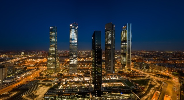 Aerial view of the illuminated Cuatro Torres Business Area skyscrapers at night with surrounding urban infrastructure and city lights in Madrid Comunidad de Madrid Spain.