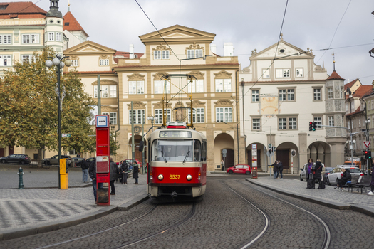 Prague Czechia 25 November 2022 View of a classic red and white tram moving along tracks past historic buildings and people at a stop in the city center.