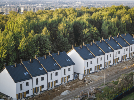 Aerial view of a row of modern white terraced houses with dark roofs under construction situated next to a lush green forest in Wieliczka Lesser Poland Voivode Poland.
