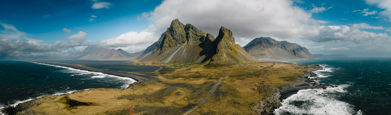 Aerial view of the dramatic Vestrahorn mountain rising above the black sand beach and rugged coastline of Stokksnes in Iceland.