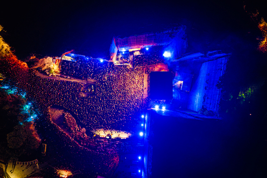 Aerial view of a large crowd gathered for an outdoor night concert with bright stage lighting and surrounding trees in Vintijan Istria County Croatia. Aerial view of a large crowd gathered for an outdoor night concert with bright stage lighting and surrounding trees in Vintijan Istria County Croatia.