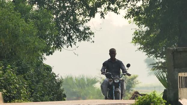 View of a man riding a motorcycle on a rural road Bangladesh.