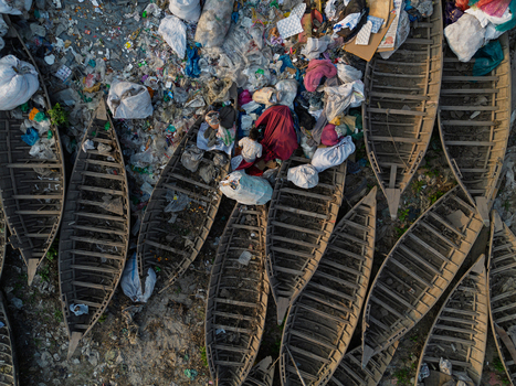 Dhaka Division Bangladesh 23 January 2026 Aerial view of wooden boats on the polluted banks of the Buriganga River with a person working among plastic waste and garbage.