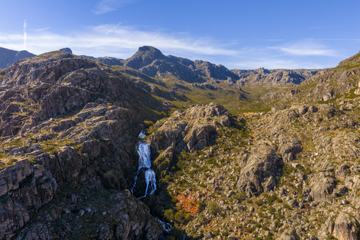 Aerial view of Vale da Candeeira waterfall cascading down rugged granite cliffs under a clear blue sky in Manteigas Distrito da Guarda Portugal. Aerial view of Vale da Candeeira waterfall cascading down rugged granite cliffs under a clear blue sky in Manteigas Distrito da Guarda Portugal.