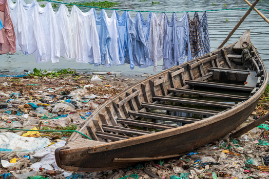 Dhaka Division Bangladesh 14 May 2026 View of a wooden boat on the trash filled banks of the Buriganga River with laundry hanging in the background.