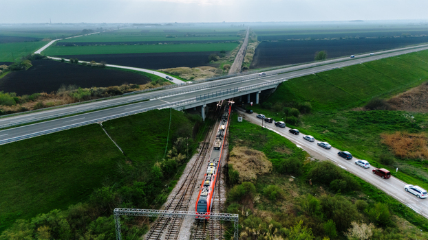 Aerial view of a long train passing under a highway bridge contrasted against the dark fields under a cloudy sky Sremska Mitrovica Vojvodina Serbia. Aerial view of a long train passing under a highway bridge contrasted against the dark fields under a cloudy sky Sremska Mitrovica Vojvodina Serbia.