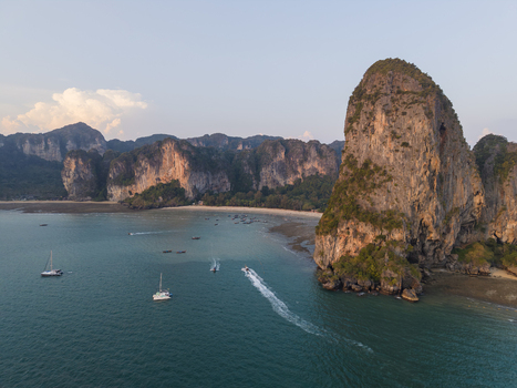 Aerial view of towering limestone cliffs meet the turquoise sea boats dotting the water under a soft golden light Krabi Thailand.