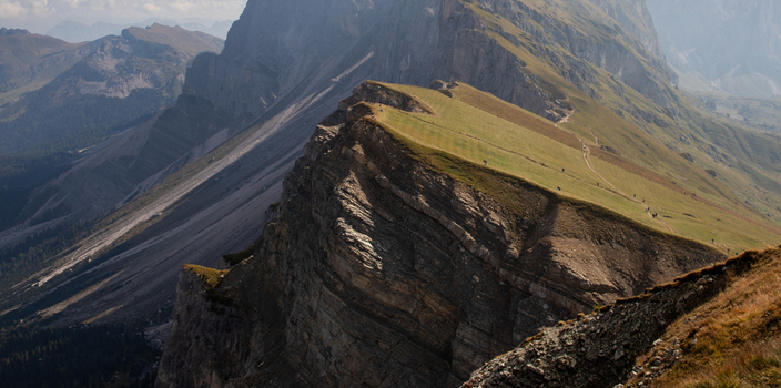 Aerial view of the Dolomites mountain range featuring steep rocky cliffs and a grassy ridge with hikers walking along a trail in Rocca Pietore Veneto Italy.