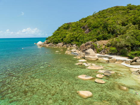Aerial view of the rocky coastline with large boulders clear turquoise water and lush green vegetation under a bright blue sky in Koh Samui Surat Thani Thailand.