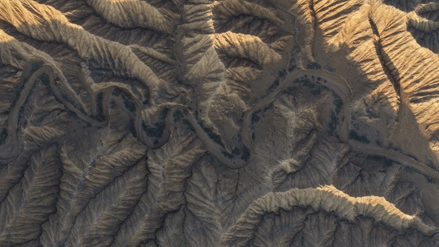 Aerial view of the winding riverbed cutting through the rugged arid landscape of the Issyk Kul area with deep shadows and textured geological formations in Issyk Kul Region Kyrgyzstan. Aerial view of the winding riverbed cutting through the rugged arid landscape of the Issyk Kul area with deep shadows and textured geological formations in Issyk Kul Region Kyrgyzstan.