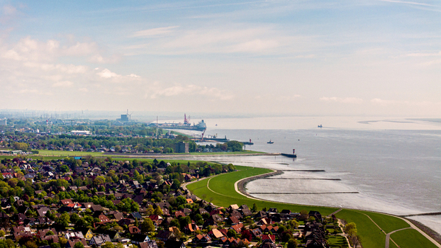 Aerial view of the town of Brunsbuttel featuring residential areas green dikes and the Elbe river estuary with industrial port facilities Brunsbuttel Schleswig Holstein Germany. Aerial view of the town of Brunsbuttel featuring residential areas green dikes and the Elbe river estuary with industrial port facilities Brunsbuttel Schleswig Holstein Germany.