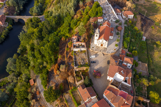 Aerial view of the historic church and red tiled rooftops of a traditional village nestled along a winding river and stone bridge Coja Coimbra District Portugal. Aerial view of the historic church and red tiled rooftops of a traditional village nestled along a winding river and stone bridge Coja Coimbra District Portugal.