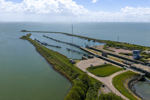Aerial view of Lorentzsluizen lock complex with green embankments calm water and wind turbines on the horizon under a cloudy sky Kornwerderzand Friesland Netherlands.