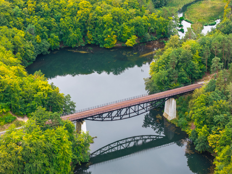 Aerial view of the Historic Railway Truss Bridge in Rutki spanning a calm river surrounded by lush green forest in Rutki Pomeranian Voivodeship Poland. Aerial view of the Historic Railway Truss Bridge in Rutki spanning a calm river surrounded by lush green forest in Rutki Pomeranian Voivodeship Poland.
