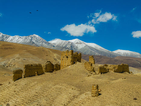 Aerial view of ancient mud brick ruins set against a backdrop of snow capped Himalayan mountains under a clear blue sky in Nepal.