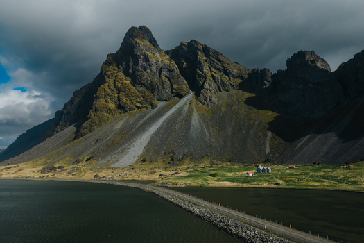 Aerial view of Stokksnes and the dramatic Vestrahorn mountain with a coastal road and dark water in Iceland.
