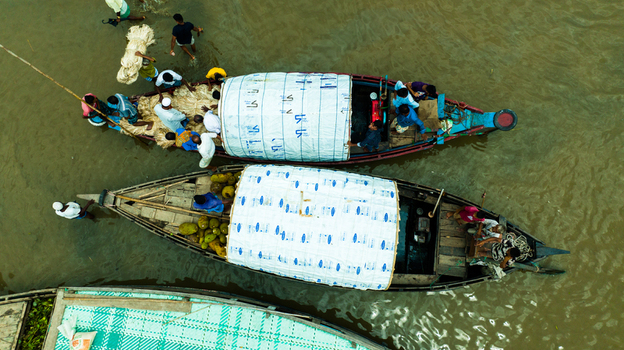 Aerial view of Baish Mowza Sarak Bazar with people loading goods onto traditional wooden boats on the river in Nabinagar Chittagong Division Bangladesh. Aerial view of Baish Mowza Sarak Bazar with people loading goods onto traditional wooden boats on the river in Nabinagar Chittagong Division Bangladesh.