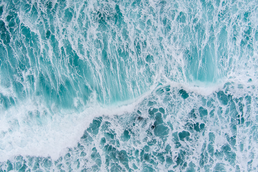 Aerial view of turquoise ocean waves with white foam crashing near the coast of Lofoten in Nordland Norway.