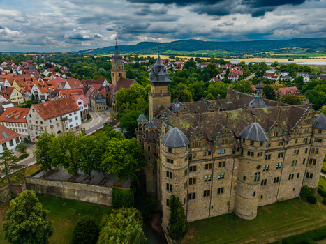 Aerial view of Schloss Neuenstein surrounded by historic town buildings lush green trees and stone fortifications under a cloudy sky in Neuenstein Baden Wurttemberg Germany. Aerial view of Schloss Neuenstein surrounded by historic town buildings lush green trees and stone fortifications under a cloudy sky in Neuenstein Baden Wurttemberg Germany.