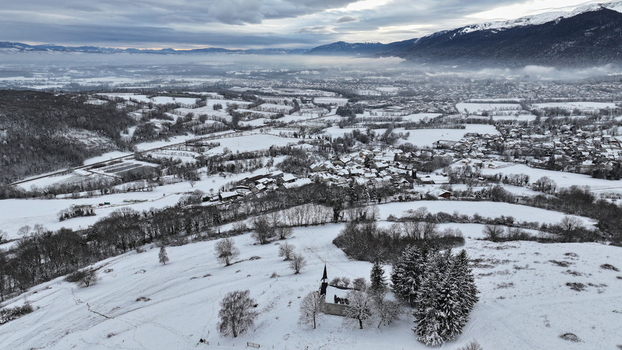 Aerial view of the snow covered village of Vesancy and the historic Chapelle de Riantmont surrounded by winter fields and mountains in Vesancy Auvergne Rhone Alpes France. Aerial view of the snow covered village of Vesancy and the historic Chapelle de Riantmont surrounded by winter fields and mountains in Vesancy Auvergne Rhone Alpes France.