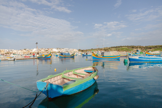 View of vibrant colorful fishing boats bobbing gently on the tranquil deep blue harbor waters under a soft sky Marsaxlokk Malta. View of vibrant colorful fishing boats bobbing gently on the tranquil deep blue harbor waters under a soft sky Marsaxlokk Malta.