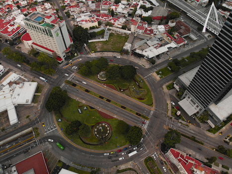 Aerial view of Glorieta Stampede featuring a circular intersection with lush green landscaping fountains and surrounding urban buildings in Guadalajara Jalisco Mexico. Aerial view of Glorieta Stampede featuring a circular intersection with lush green landscaping fountains and surrounding urban buildings in Guadalajara Jalisco Mexico.