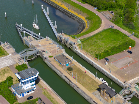 Aerial view of the Lorentzsluizen lock system with a sailboat navigating the canal next to green embankments and control buildings Kornwerderzand Friesland Netherlands.
